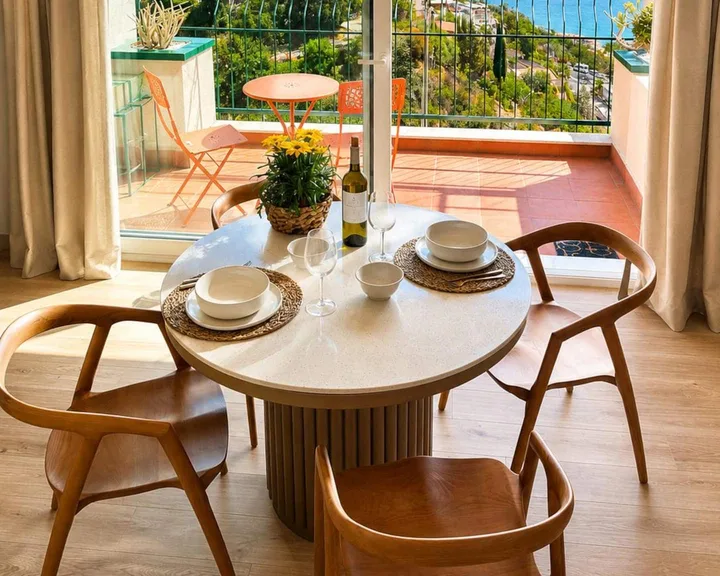 Il tavolo rotondo apparecchiato, con il terrazzo e il mare oltre la vetrata